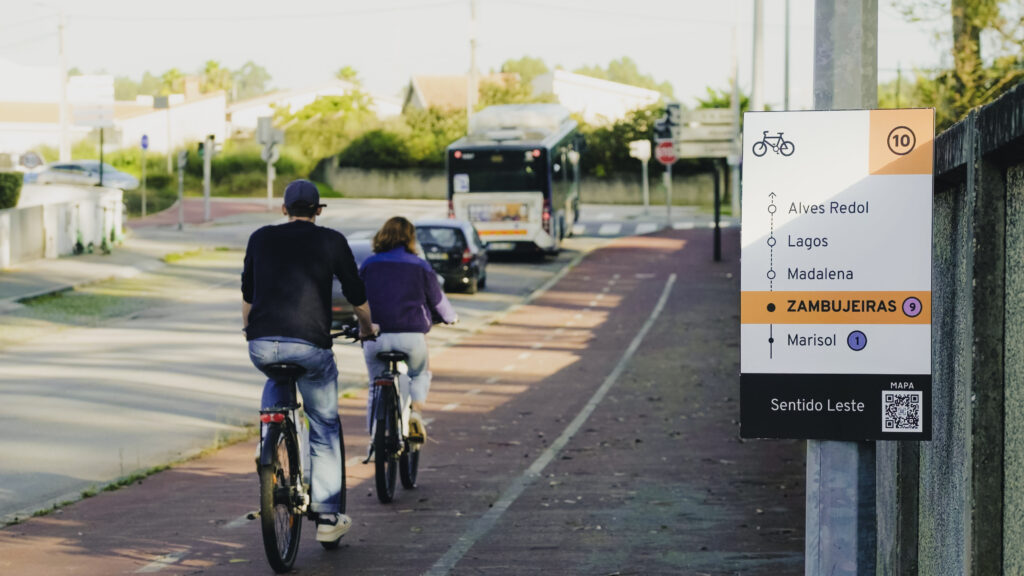 two people biking on a cycle path with a sign that gives wayfinding information in the foreground